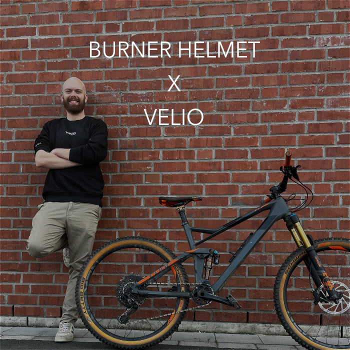 BURNER HELMET X VELIO Mann lehnt sich vor einem Ziegelsteinwand mit einem Fahrrad